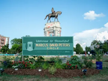 The Robert E. Lee Monument stands on a tall stone base covered in graffiti, with a green Marcus-David Peters Circle sign in the foreground.