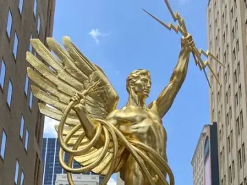 Golden Boy statue of a winged male figure holding lightning bolts and a coiled cable in Dallas.