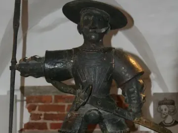 Old Thomas statue in armor with a wide-brimmed hat, mustache, sword, and long pole-like weapon.