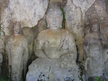 Three weathered stone Buddhas carved into a light grey cliff face at Usuki Stone Buddhas.