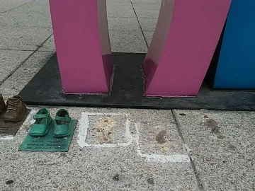 Antimonumento 49 ABC with small sculptural shoes placed on the pavement beside faded painted square outlines.