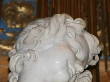Close-up of the Ecstasy of Saint Teresa sculpture showing a white marble face with curled hair and a serene expression.