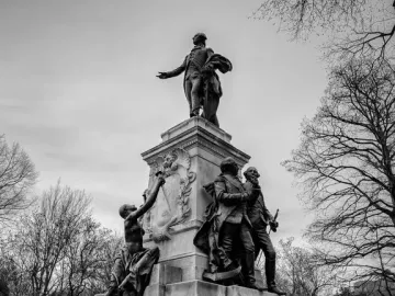The Marquis de Lafayette statue rises on a multi-tiered pedestal with smaller figures at the base, photographed in black and white against bare trees and an overcast sky.