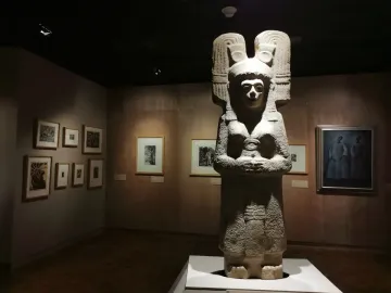 The Young Woman of Amajac stone statue standing in a museum gallery with an ornate headdress and clasped hands.