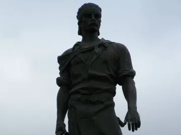 Laçador statue of a man holding a coiled lasso against an overcast sky.