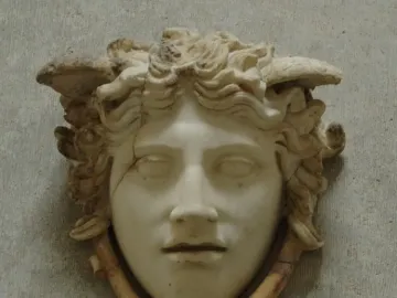 Medusa Rondanini marble head with curly hair and wing-like elements against a grey wall.