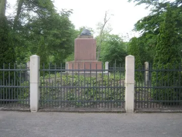 Napoleonstein stone monument behind a dark metal fence in a leafy park.
