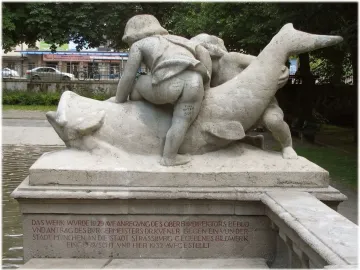 Rhine Water Fountain sculpture with two youthful figures and a large fish-like creature, with red inscription on the base.