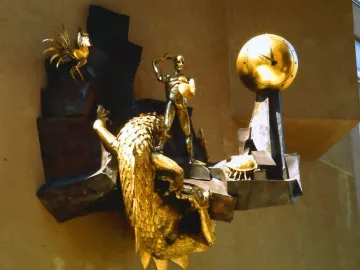The Defender of Time sculpture with a golden figure, clock, rooster, and creature mounted on a wall.