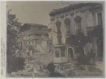 John of Austria statue on a tall pedestal amid rubble beside a damaged building