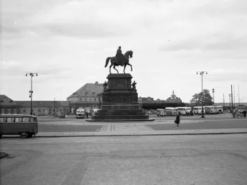 King Johann Memorial equestrian statue on a stone pedestal in a city square with buses and pedestrians nearby.