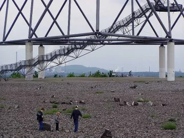 Visitors climb the stairway of the Tetrahedron steel lattice structure, with children exploring the rocky base below.