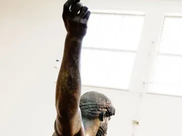 The Artemision Bronze seen from the side and back, with one arm raised and the other extended.