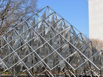 Delta Solar pyramid sculpture made of a metallic grid with reflective triangular panels, set against bare trees and a light-colored building.