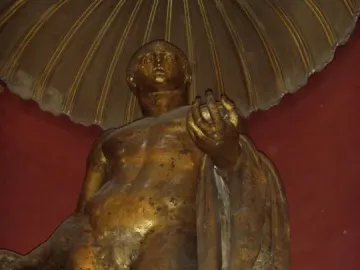 Weathered bronze statue of Hercules standing nude, holding a staff and apples with an animal skin draped over one arm.