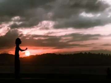 La Madre del emigrante silhouetted against a colorful sunset over the sea.