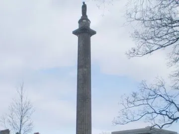 The Melville Monument rises from St Andrew\'s Square Gardens beside paved walkways and lawn, with people walking nearby.