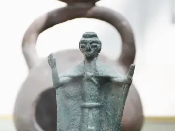 Nuragic bronze statuette of a tribal chief with a raised arm and staff, mounted on a wooden base.