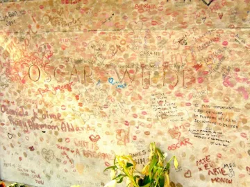 Oscar Wilde’s tomb covered with lipstick imprints, handwritten messages, and drawings, with flowers at the base.
