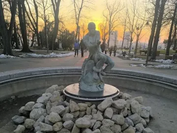 Fisherman Fountain statue in a park at sunset, with a man wrestling a snake in the center of a dry circular basin.