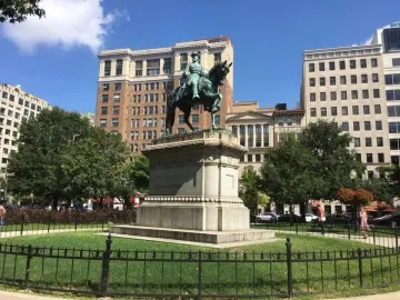 Major General James B. McPherson Memorial equestrian statue on a tall pedestal in a grassy park with city buildings behind it.