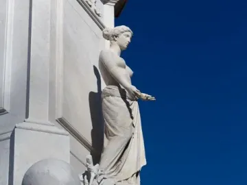 Peace Monument with a draped marble female figure and carved base against a blue sky.