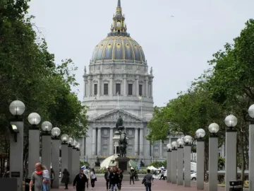 Pioneer Monument on a granite base in a brick-paved plaza, with San Francisco City Hall and its dome in the background.