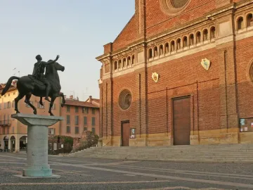 Regisole equestrian statue on a pedestal in a paved square with the cathedral of Pavia behind it.