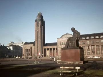 The Aleksis Kivi Memorial, a dark seated statue of a bowed man on a reddish-brown pedestal in a city plaza.