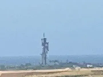 Birth of the New World sculpture silhouetted in the hazy distance above a bright landscape and water