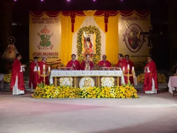 Black Nazarene statue in red and gold robes carrying a cross beneath a floral archway