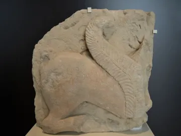 Weathered stone relief of the El Salobral Sphinxes shown in profile, with a large textured wing curving upward across the figure.