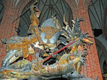Saint George and the Dragon sculpture showing a knight in golden armor on a grey horse battling a dragon inside a church