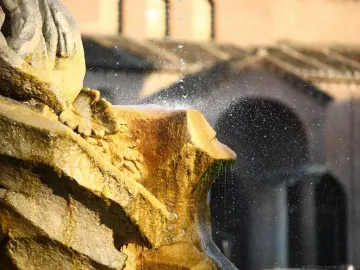 Weathered stone section of the Fountain of the Tritons with water spraying and dripping over green algae.