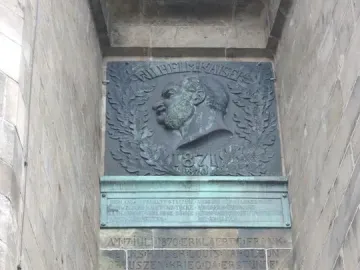 Bronze plaque on the Hermannsdenkmal showing a relief bust of a bearded man in profile, framed by a laurel wreath and the year 1871, with carved German inscription below.