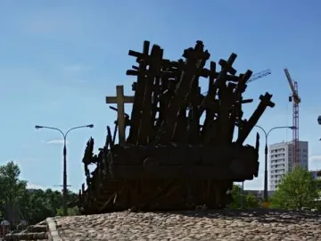 Monument to the Fallen and Murdered in the East, a dark sculpture of crosses and wooden beams on a raised cobblestone platform, with an inscribed stone in front.