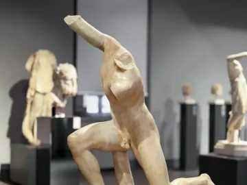 Subiaco Ephebe, a pale stone kneeling male sculpture displayed on a dark pedestal in a museum gallery.