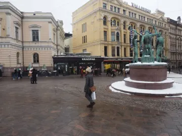 The Three Smiths sculpture on a snow-dusted pedestal in a busy Helsinki square.