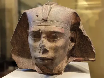 Weathered stone head of the Djedefre sphinx with a damaged nose and worn headdress edges.