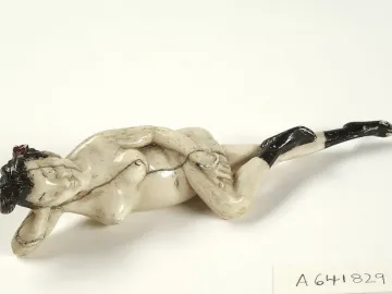 Doctor\'s Lady ivory figure reclining on its side, with dark hair, black-painted feet, and a small red hair adornment.