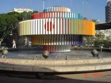 Fire and Water Fountain with colorful vertical slats spraying water into a circular basin, with a faint rainbow in the mist.