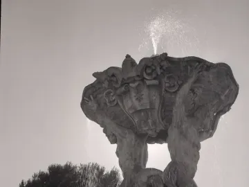 The Fountain of the Tritons with two muscular figures supporting a shell-shaped basin as water sprays upward and cascades down.