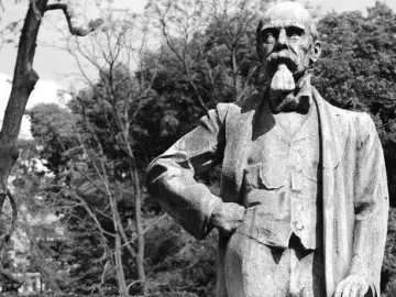 Stone monument to Ernesto Teodoro Moneta showing a standing man on a pedestal in a park.