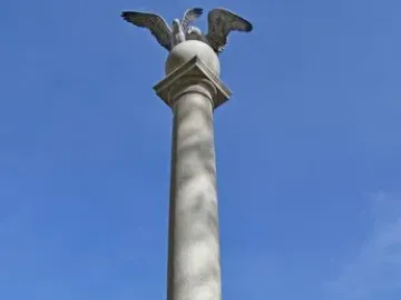 Seagull Monument with twin bird sculptures on a stone pedestal, framed by flowers against a blue sky.