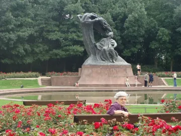 Chopin Monument in Warsaw surrounded by red roses, with people gathered around a reflecting pool.