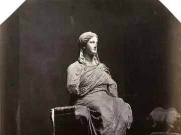 Demeter of Knidos, a draped seated statue with broken arms, photographed against a dark background.