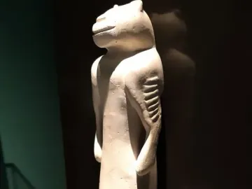 Lion-man sculpture with an animal-like head and slender human-shaped body, shown against a dark background.