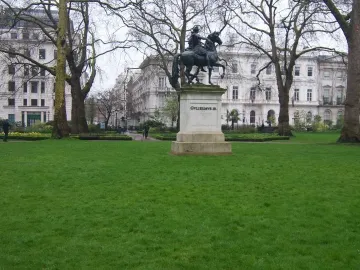 William III equestrian statue on a light-colored pedestal in a grassy park, with trees and buildings behind it.