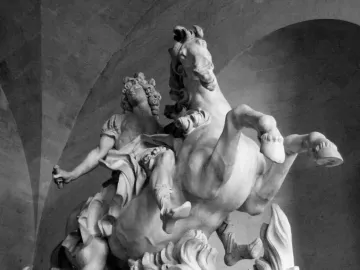 Equestrian Statue of Louis XIV shown as a marble rider on a rearing horse beneath a dark arched ceiling.