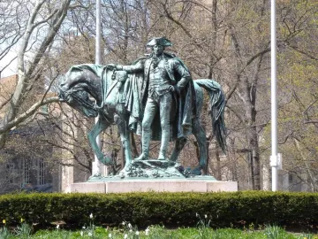 George Washington statue on a granite base with a horse beside it, framed by hedges and bare trees.